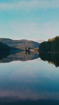 Scenic calm water drone view at Sherman Reservoir Boat Launch, Vermont, USA, with forested mountains, tree reflections and clear sky. Peaceful nature and boating recreation. 4K. Slow dolly. Vertical.