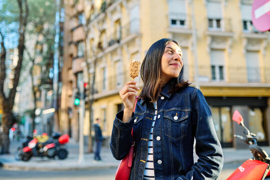 Portrait of a smiling young woman girl eating an ice cream walking in the city, tourists visiting destination, summer trip exploring