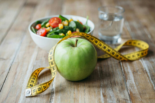 Healthy woman in kitchen preparing fresh green apple and salad with measuring tape