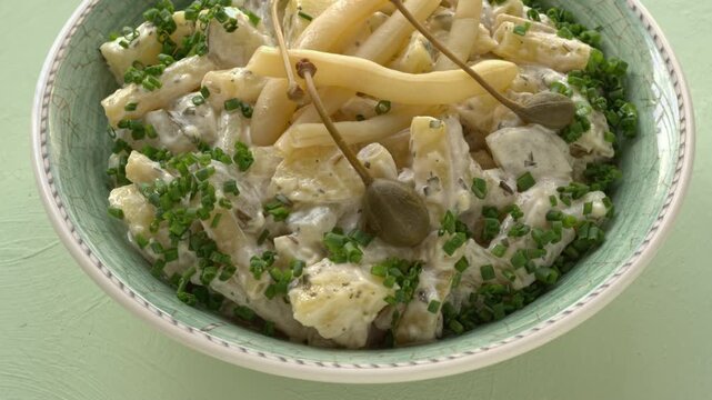 Potato salad with a twist: replace pickled cucumbers with fermented yellow snap beans and top with caper berries. Pastel green background, table spin.