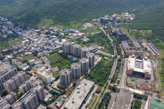 Aerial view of Hinjewadi Phase III featuring modern residential high-rise buildings and commercial office complexes surrounded by lush green hills in Pune, Maharashtra, India.