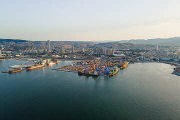 Obraz premium Commercial harbor with container terminal and cargo handling cranes. Drone view of maritime logistics, freight transportation and coastal industry