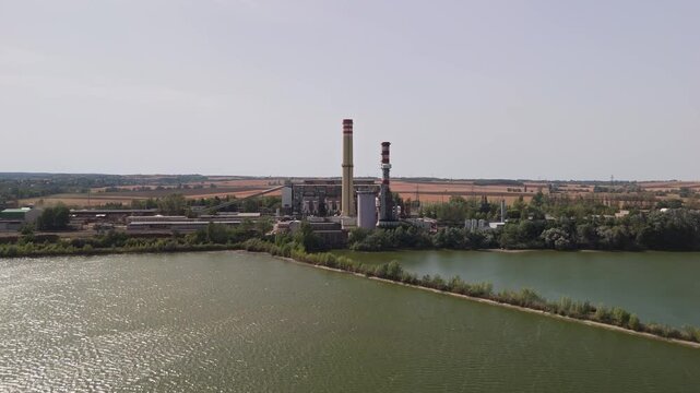 Lake Bokod in Hungary with the Bokodi cooling lake, biomass and coal power plant, cooling towers, transmission lines and forested rural landscape in an aerial view.