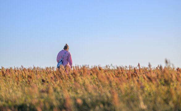 Solitary woman walking through golden coastal meadow at dusk.