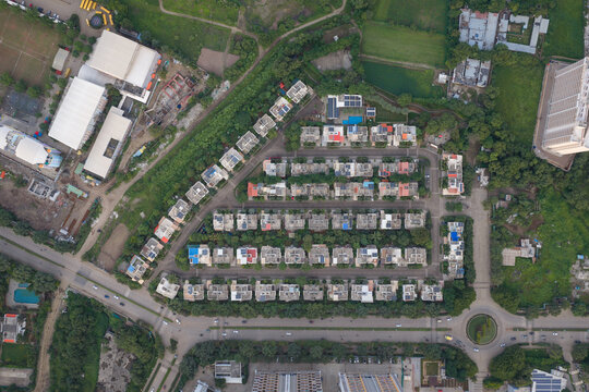 Aerial view of a modern residential housing complex with rows of houses, green spaces, and a nearby roundabout in Pune, Maharashtra, India.