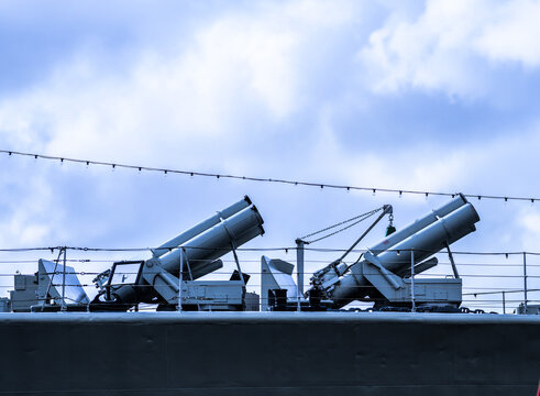 Naval ship deck guns silhouetted against dramatic cloudy sky.