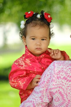 Adorable Asian baby girl in traditional red silk dress outdoors wearing cute hair accessory