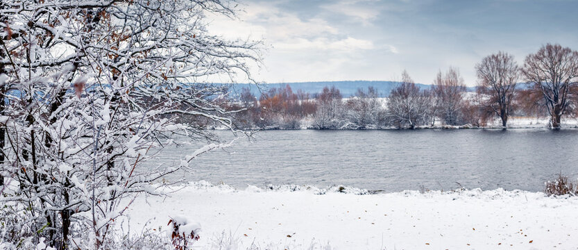 Winter landscape with river, snow covered trees and hills in background