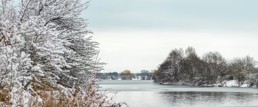 Winter landscape with lake, snow covered trees and cloudy sky in background