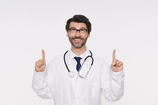 Doctor man wearing coat and stethoscope with pointing up advertisement logo in studio isolated white background. Healthcare, medical professional, life insurance, ad offer, medicine promotion