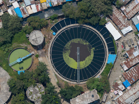 Aerial view of PCMC Waste Water Treatment Plant featuring large circular sedimentation tanks with green algae and surrounding urban infrastructure in Pimpri-Chinchwad, Maharashtra, India.