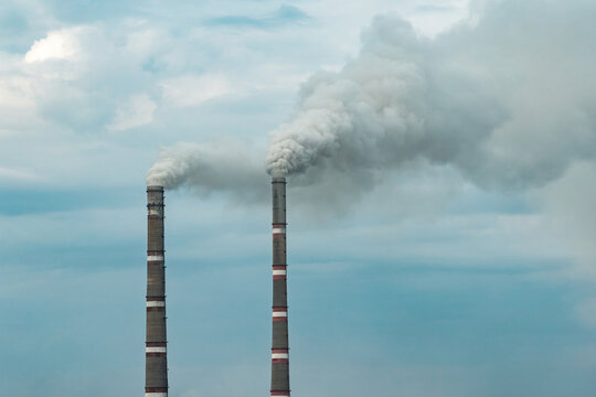 Two industrial chimneys releasing large plumes of smoke into the atmosphere.