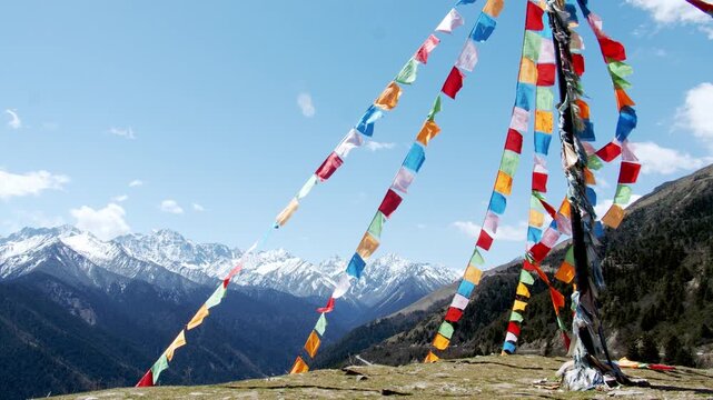 Colorful prayer flags on a mountain ridge with snowy Himalayan peaks and blue sky in Himalayas