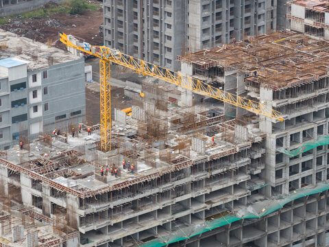 Aerial view of a construction site in Punawale featuring a yellow tower crane, workers on the concrete structure, and residential buildings in Pimpri-Chinchwad, Maharashtra, India.