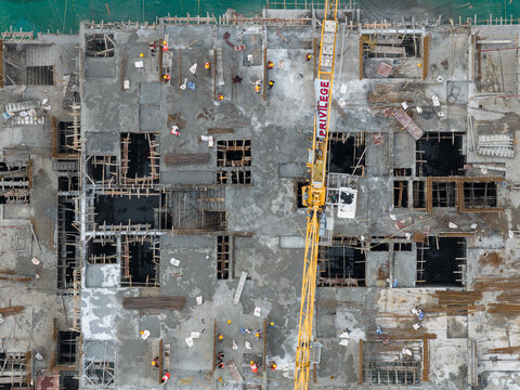 Aerial view of the Punawale construction site featuring a yellow crane, concrete slabs, exposed rebar, and workers in hard hats in Pimpri-Chinchwad, Maharashtra, India.