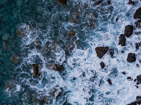 Clear ocean water with waves breaking over coastal rocks. Aerial top view of Atlantic shoreline with foam and stone texture