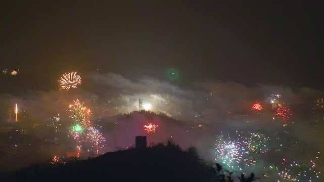Fireworks exploding over a misty mountain town skyline at night