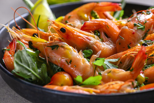 Fresh cooked shrimp with garlic, parsley and lemon on a black plate, top view, dark stone background.