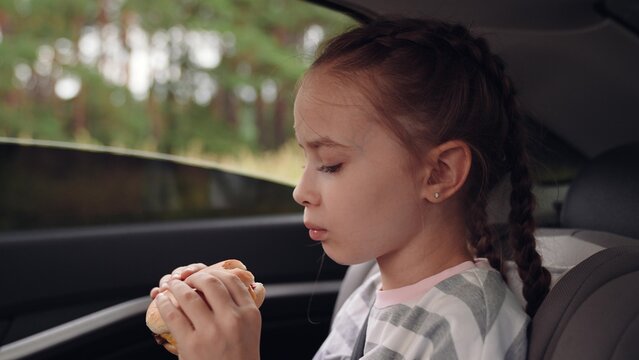 little girl child eating burger in car, happy person, Enjoying food on the road, bite by bite, sitting safely in car seat, burger in small hands, girl s fast food delight, family outing lunch, scenic
