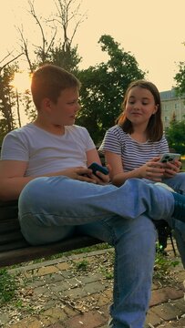 Childhood in the digital age, Youngsters bonding outside, Sunset with friends, Sharing stories with friends, Casual outdoor hangout, Smiling kids on a bench, Peaceful evening talk, Kids dressed in