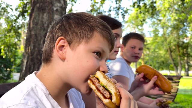 school children eat big hamburger, kids eat burger park, group children friends eat cutlet bun, Happy youths enjoying food, friendly conversation in the park, classic picnic scene, lunch break on a