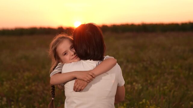Mother and daughter hug at sunset, Family love in the evening sun, Warm embrace in nature, Parenting moments outdoors, Child comforted by parent, Emotional sunset bonding, Tender moments in a field