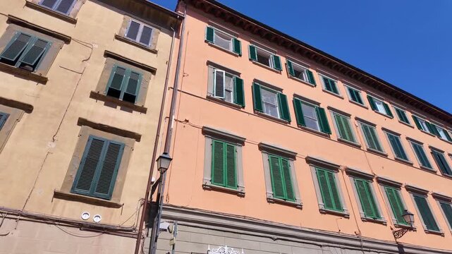 Pan across pastel building facade with green shutters, italy