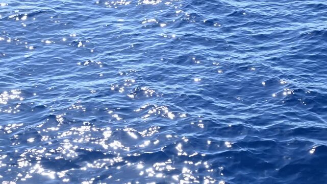 Sunlight sparkling on open water with gentle waves while the boat is moving