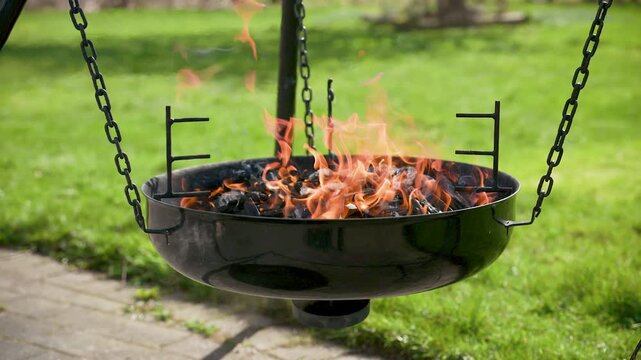 Hanging black barbecue grill filled with burning charcoal outdoors