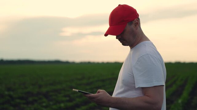 Agriculture, Field survey with technology, Modern day farmer s routine, Red cap farmer with phone, Soil inspection with digital tools, Farm tech trends, Connected devices in agriculture, Man planning