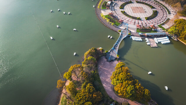 Aerial view of Century Park featuring a pedestrian bridge connecting a lush green island to a circular plaza, with small boats on the lake in Shanghai, Shanghai, China.