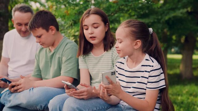 scrolling through apps under leafy trees., kids browsing phones in a green garden, children absorbed by screens among trees, children checking messages on their phones, sunlight filters through leaves