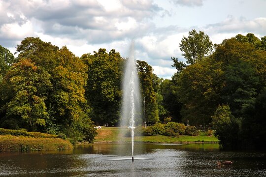 Wiesbaden, Hesse, Germany: Fountain rising from pond in Kurpark surrounded by lush trees and landscaped greenery.