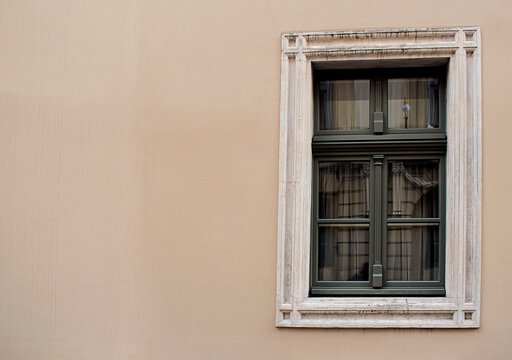 Vintage window with a dark wooden frame and decorative stone surround on the facade of a historic European building. Minimalist architectural composition with generous copy space on the beige wall, su