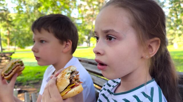 school children eat big hamburger, kids eat burger park, group children friends eat cutlet bun, Teenagers burger break in the park, outdoor meal with friends, summer holiday adventure, relaxing in