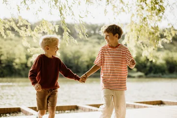 Two joyful boys exploring nature by the lake, hand in hand, on a sunny day © BGStock72
