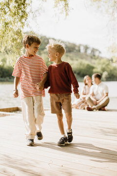 Two boys joyfully walking hand in hand along a lakeside boardwalk
