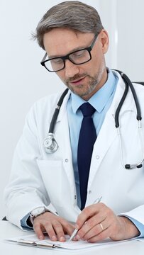 Experienced male doctor wearing a white lab coat and stethoscope. Writing details on a clipboard. Representing medical consultation. Healthcare services