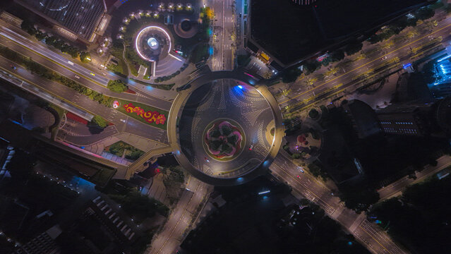 Aerial view of the Lujiazui pedestrian bridge at night, featuring circular architecture, illuminated roads, and vibrant landscaping in Shanghai, China.