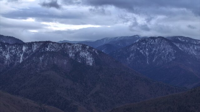 Aerial view of the snow-capped mountains near Khashuri, featuring forested slopes under a dramatic cloudy sky in Khashuri, Shida Kartli, Georgia.