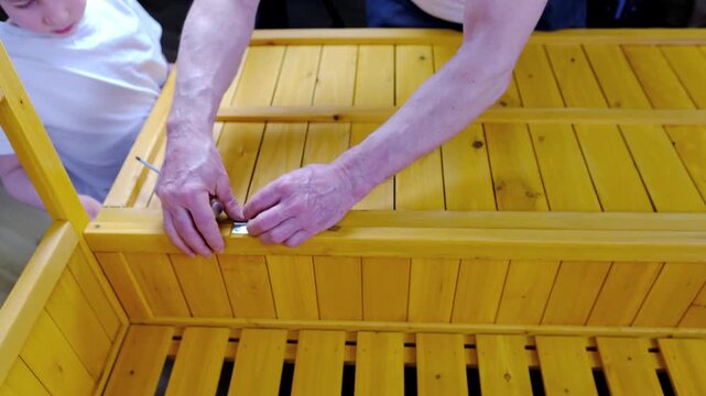 adult man 55-60 years old with son, child 9-10 years assemble wooden furniture from parts together at home, assembling garden bench with their own hands, concept to convey experience, happy family