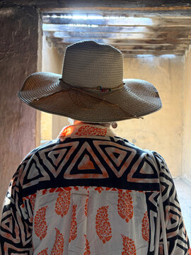 mujer con sombrero de espaldas mirando el interior de una habitaci&oacute;n vac&iacute;a iluminada IMG_5503-as26