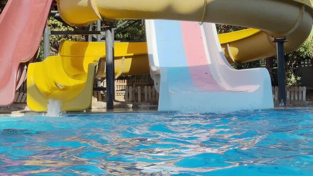 boy teenager sliding down yellow water slide splashing into blue swimming pool aquapark waterpark summer vacation fun outdoor recreation amusement park attraction leisure tourism activity