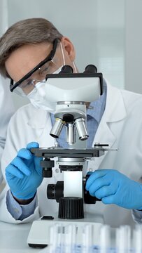 Scientist in laboratory wearing protective gear and blue gloves, meticulously adjusting a microscope for scientific research, analysis, and medical discovery