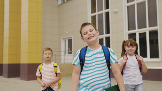 Optimism on their way to classroom, Swinging backpacks and smiling faces, Friends sharing school adventures, Colorful building as the background, Everyday life of urban school students, Diverse group