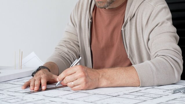 Architect hands drafting precise building plans on blueprints with ruler and pencil, demonstrating detailed architectural planning, measurement and professional design work at desk