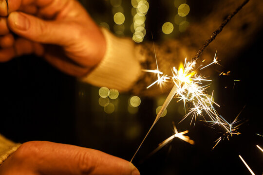 Happy new year eve. Burning Sparkler Held by Hands with Golden Bokeh Garland Background. Togetherness and New Year celebration.