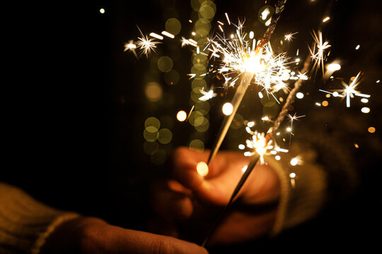 Happy New Year celebration. Close Up of Hands Holding Burning Fireworks Sparklers with Warm Golden Lights Bokeh Background on New Year Eve