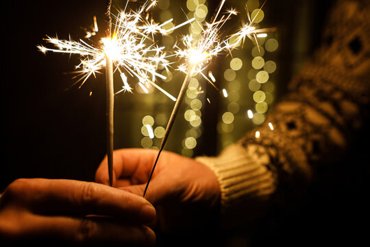 New Year celebration. Couple Holding Bright Sparklers Close Up with Warm Festive Bokeh Lights in Background. magic moments, happy new year and holiday cheer