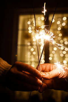 Happy new year celebration. Hands Holding Burning Sparklers with Golden Bokeh Lights Background on New Year Eve. Vertical Close Up